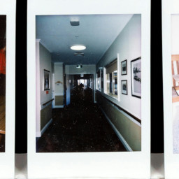polaroid square, photograph of long dark hallway with artwork on wall.