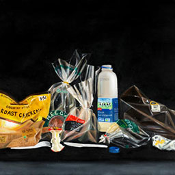 collection of grocery plastic wrapping and waste, roast chicken plastic, empty milk carton, apple core.