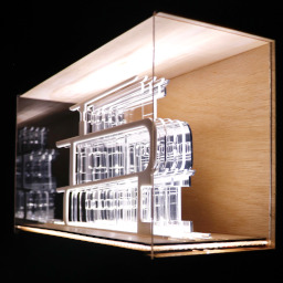 3D geometric acrylic model, curved features in a glass case with wooden back under LED lights.