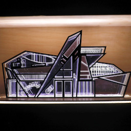 3D geometric acrylic model, angular features and blue tones, in a glass case with wooden back under LED lights.