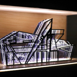 3D geometric acrylic model, angular features and blue tones, in a glass case with wooden back under LED lights.