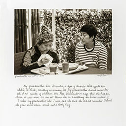 two women sitting next to each other, one older woman eating from a tray of food, the other woman watching her eat, cursive text below, black and white photograph.