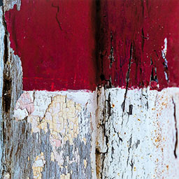 red and white paint eroding on wooden surface.