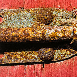 close-up orange rusted lock with bolts on red painted wood surface.