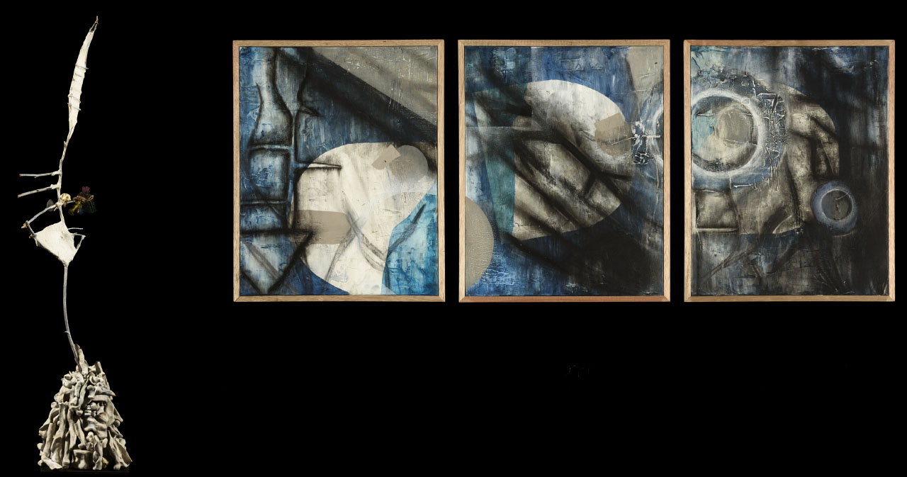 three abstract panels with circular features and shaded lines in tones of blue and off-white and a tall abstract statue made of sticks, rocks and fabric. 