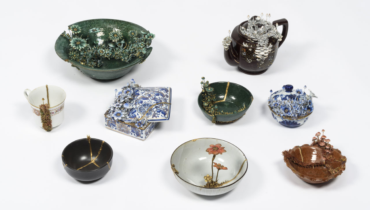 nine small ceramic vessels in greens, blues and browns with floral detail.