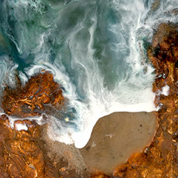 aerial photograph of waves rushing into the beach surrounded by a border of rock