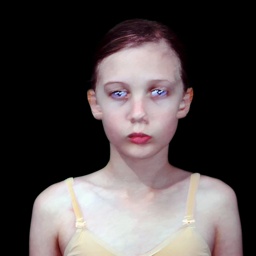 blurred photograph of young girl with pale skin and blue eyes staring straight ahead with blank expression