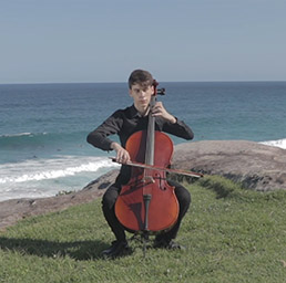 Potrait of a male holding the end of a cello with a blue background